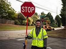 A young traffic control worker smiles while holding a stop sign on site of his highway construction career in Georgia