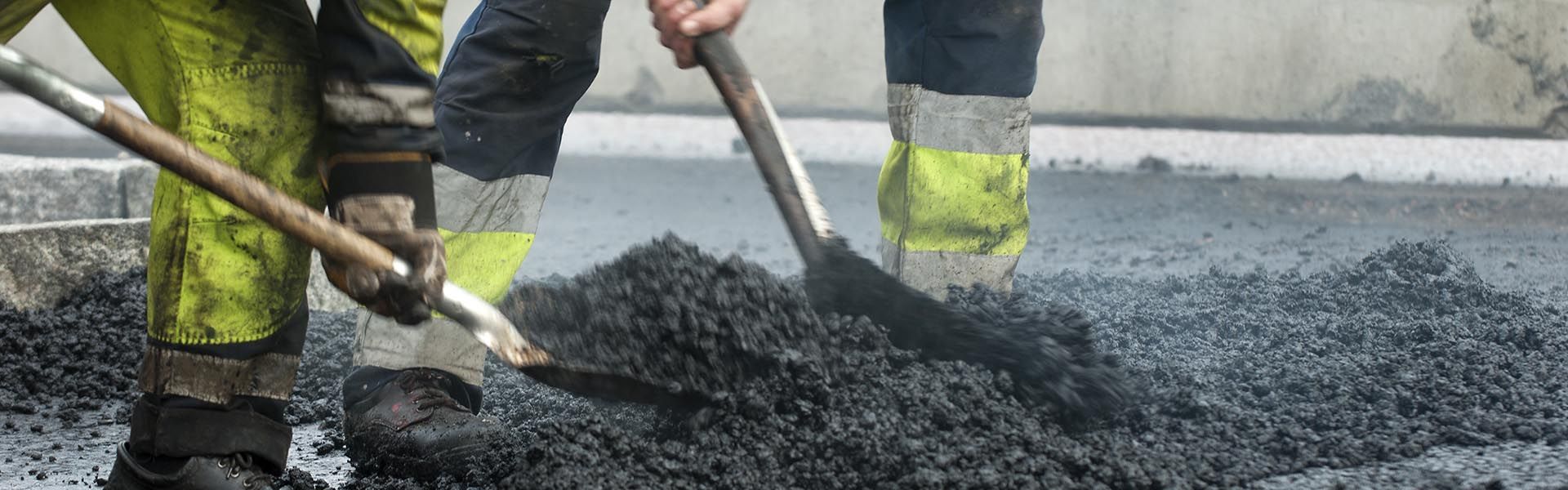 An asphalt paving worker scoops asphalt in his construction labor job