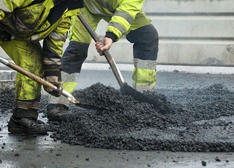 two asphalt paving workers shovel at their job site where they enjoy their highway construction career in Georgia