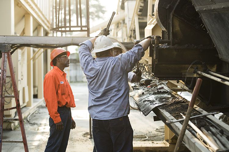 Three road construction workers discuss how to best fix the heavy equipment they all use during their construction careers