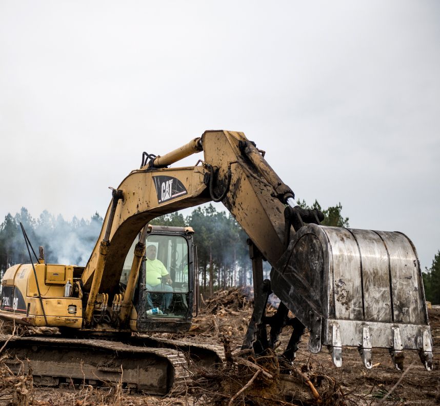 A crane, a piece of heavy equipment machinery, clears away branches to help start a paving job in Georgia