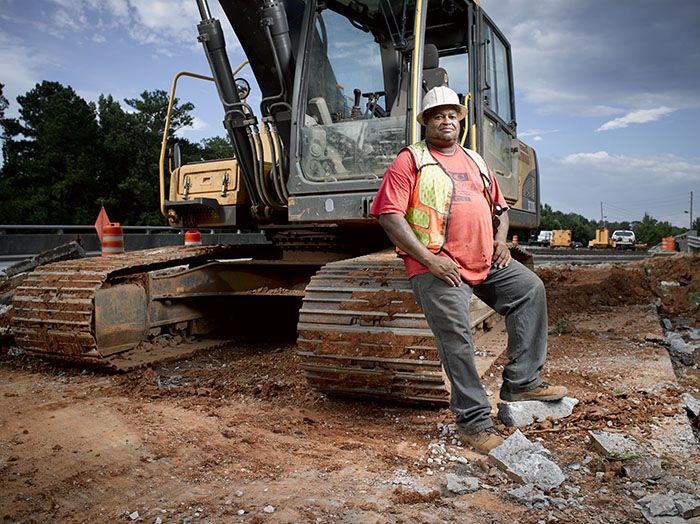 Sitting near a yellow crane on a construction site, Gino Willis smiles thinking about his construction career in Georgia.