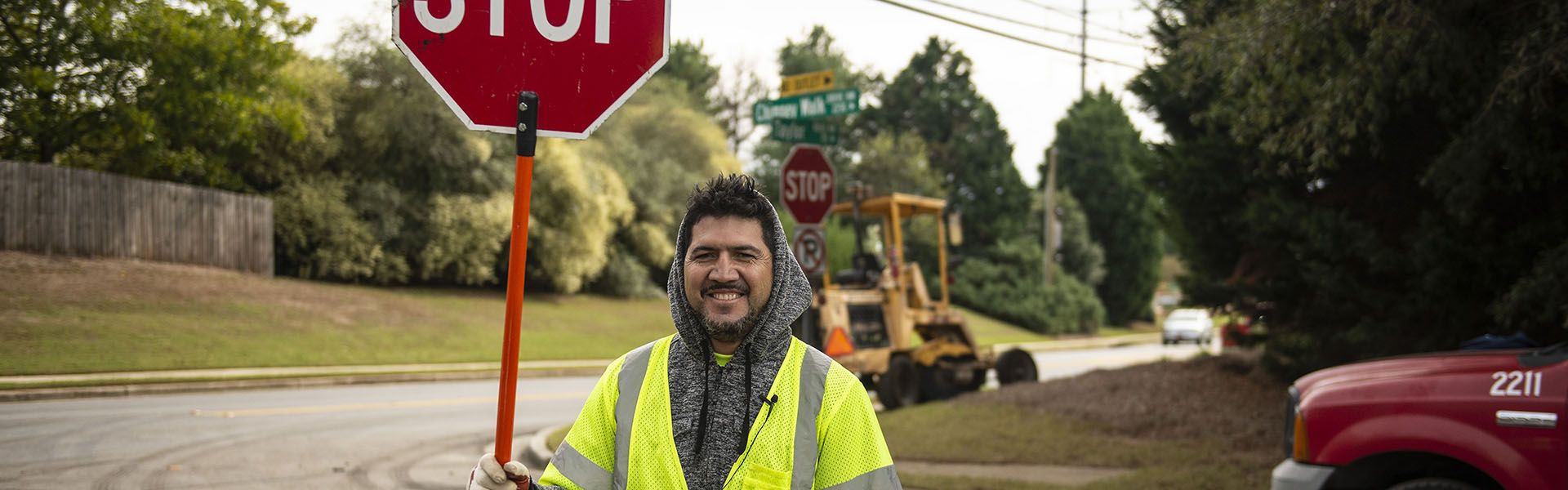 A young road construction worker smiles while holding a stop sign on site of his highway construction career in Georgia