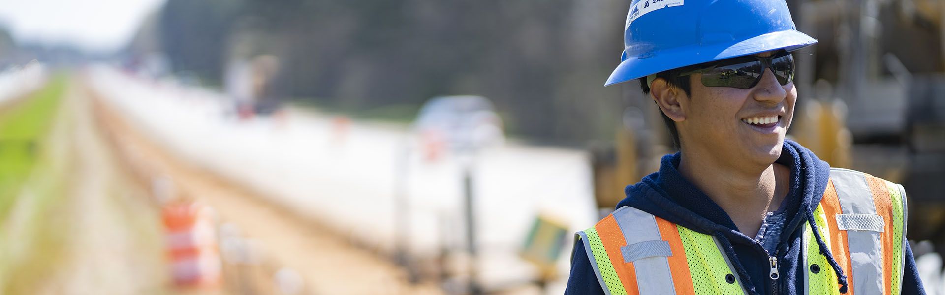 Young man smiling on site of his Georgia construction career wearing a blue construction helmet 