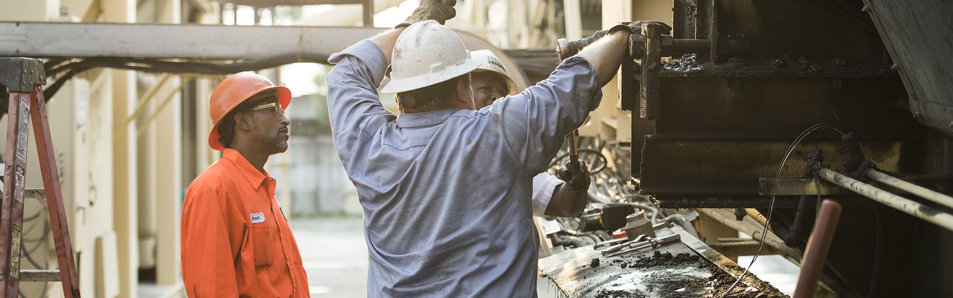 Three construction workers work on a piece of heavy equipment on a road construction job site in Georgia