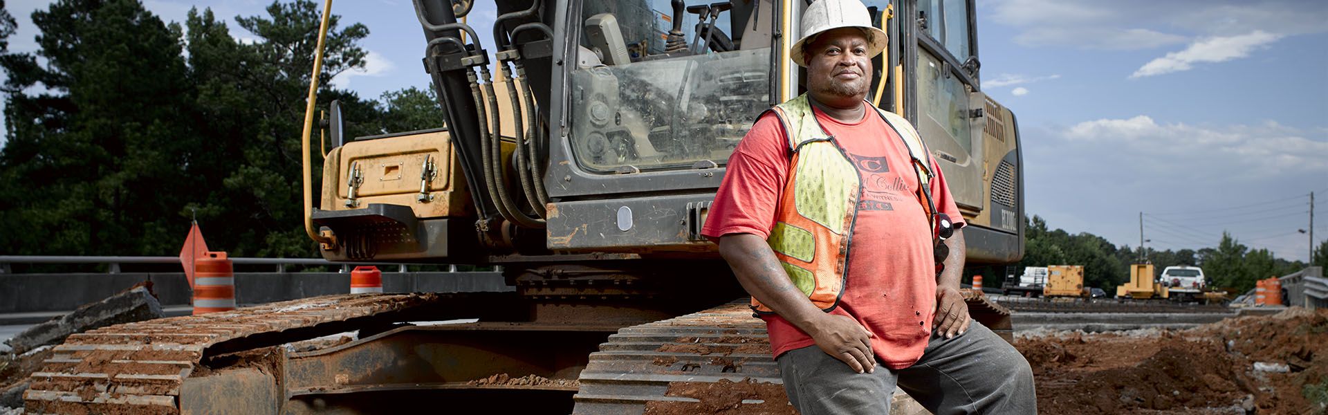 A construction worker smiles nears a piece of heavy equipment he operates as a heavy equipment operator in Georgia