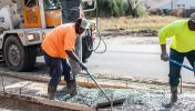 Two asphalt paving workers use a smoothing tool on the wet concrete on site of their construction careers in Georgia