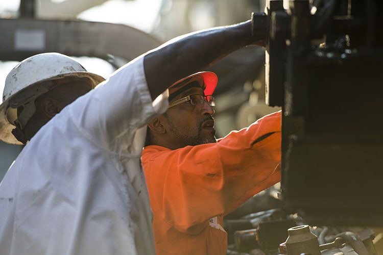 Two road construction workers work on a piece of heavy equipment on site of their construction careers in Georgia 